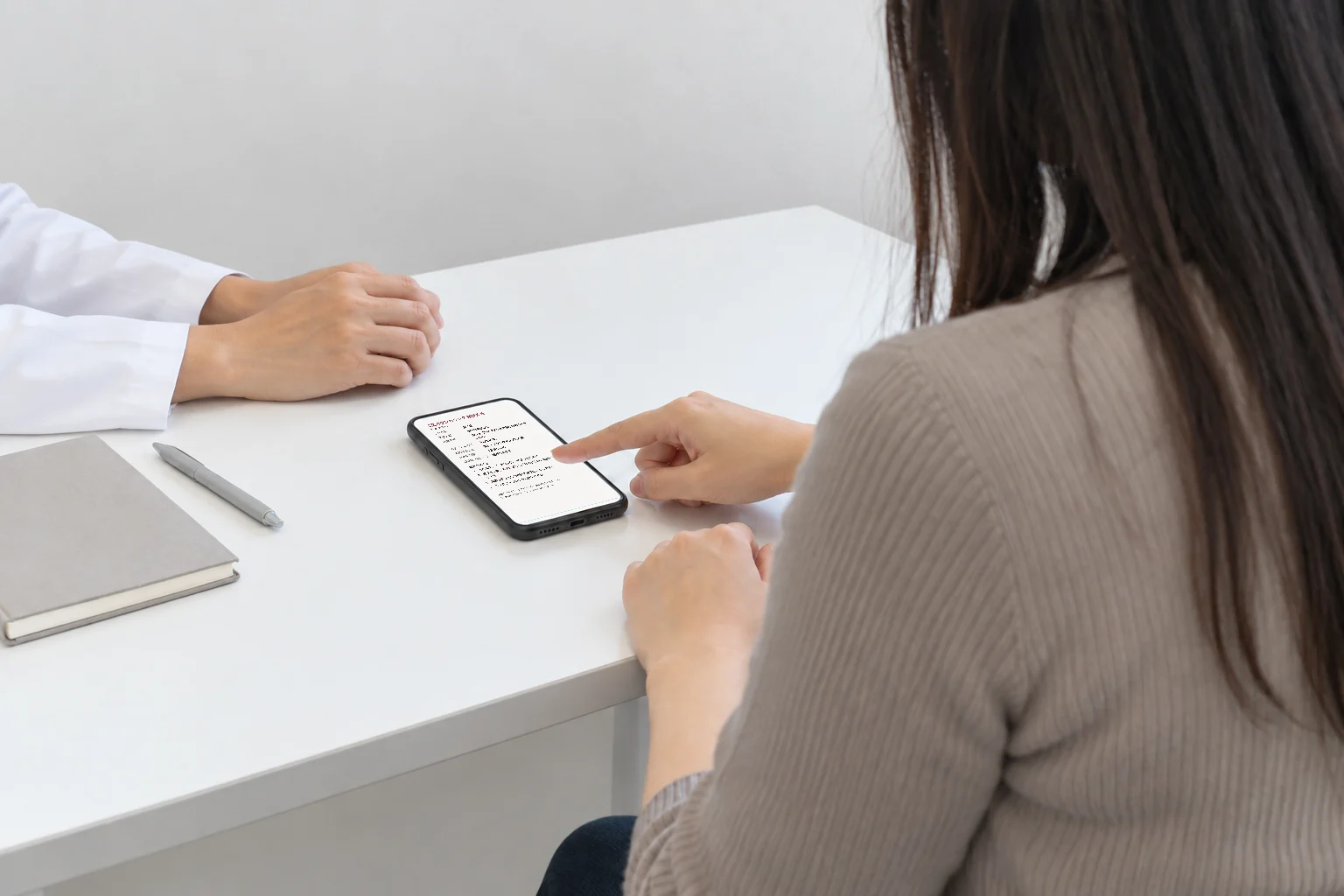 机に置いたスマホの相談メモを指さして見せている様子
